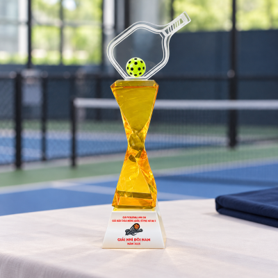 Minh họa một cúp pickleball thân vàng đặt trên bàn chuẩn bị trao giải gần sân thể thao